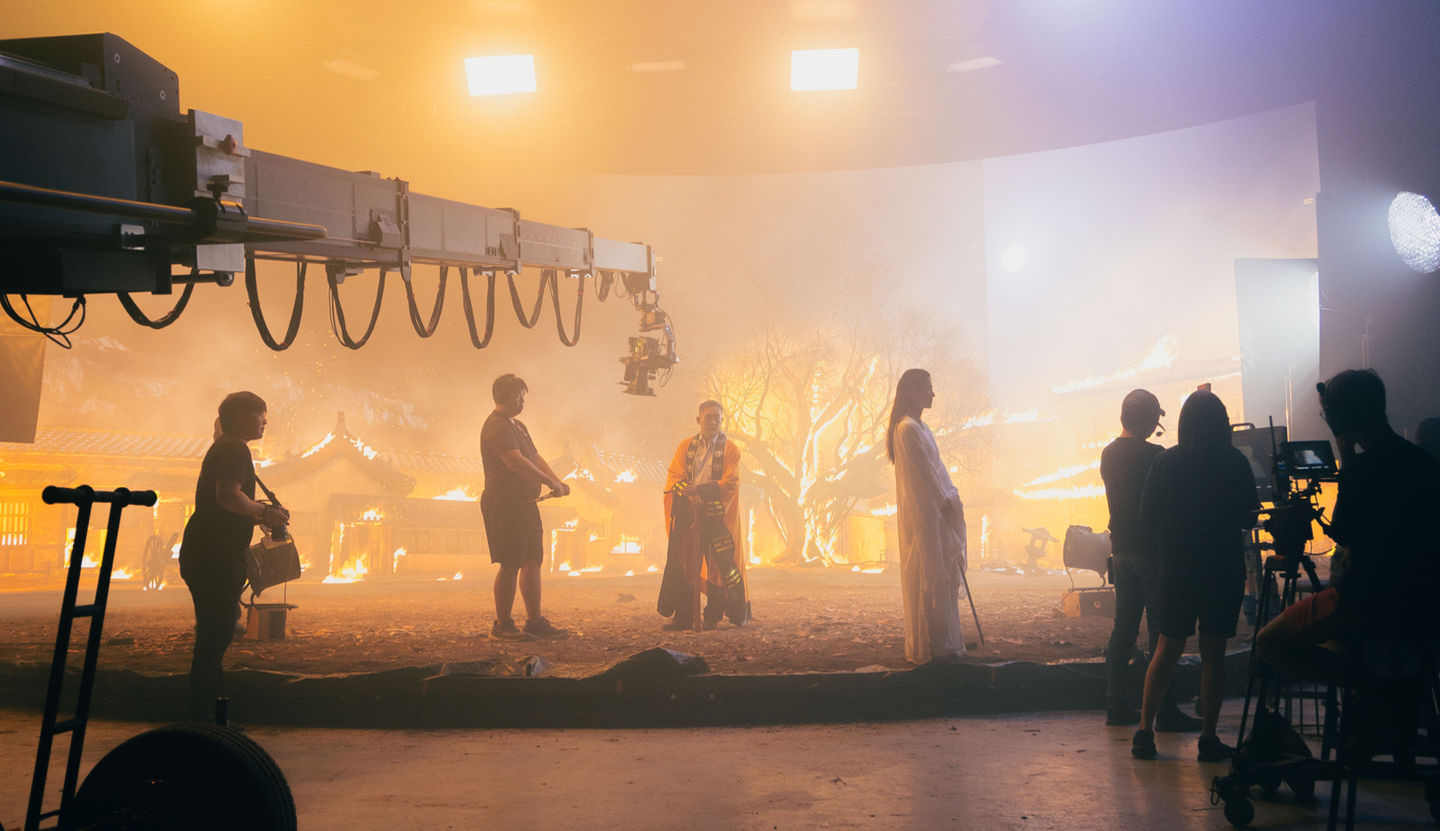 Spirit Slayer production on the X3D LED volume — crew, crane, and actors in costume with a burning village environment on the LED wall